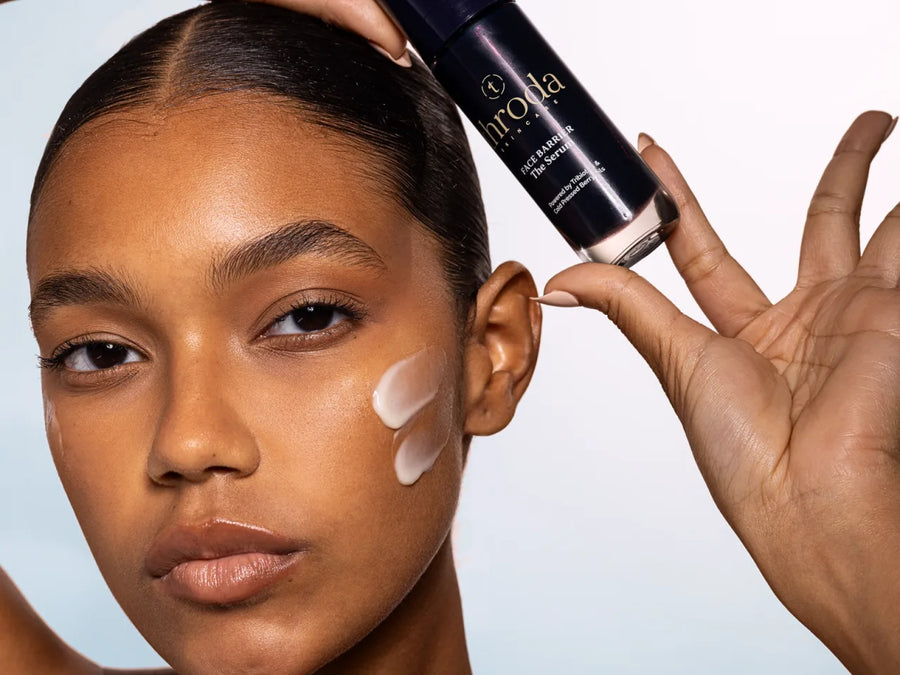 A model holding the serum bottle with cream swept across her cheek