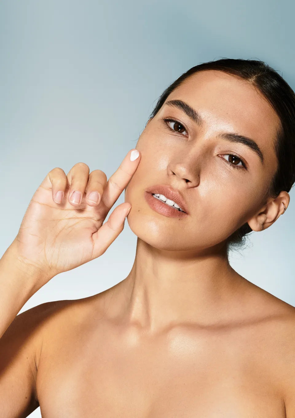 A model touching her cheek, skin bare and even